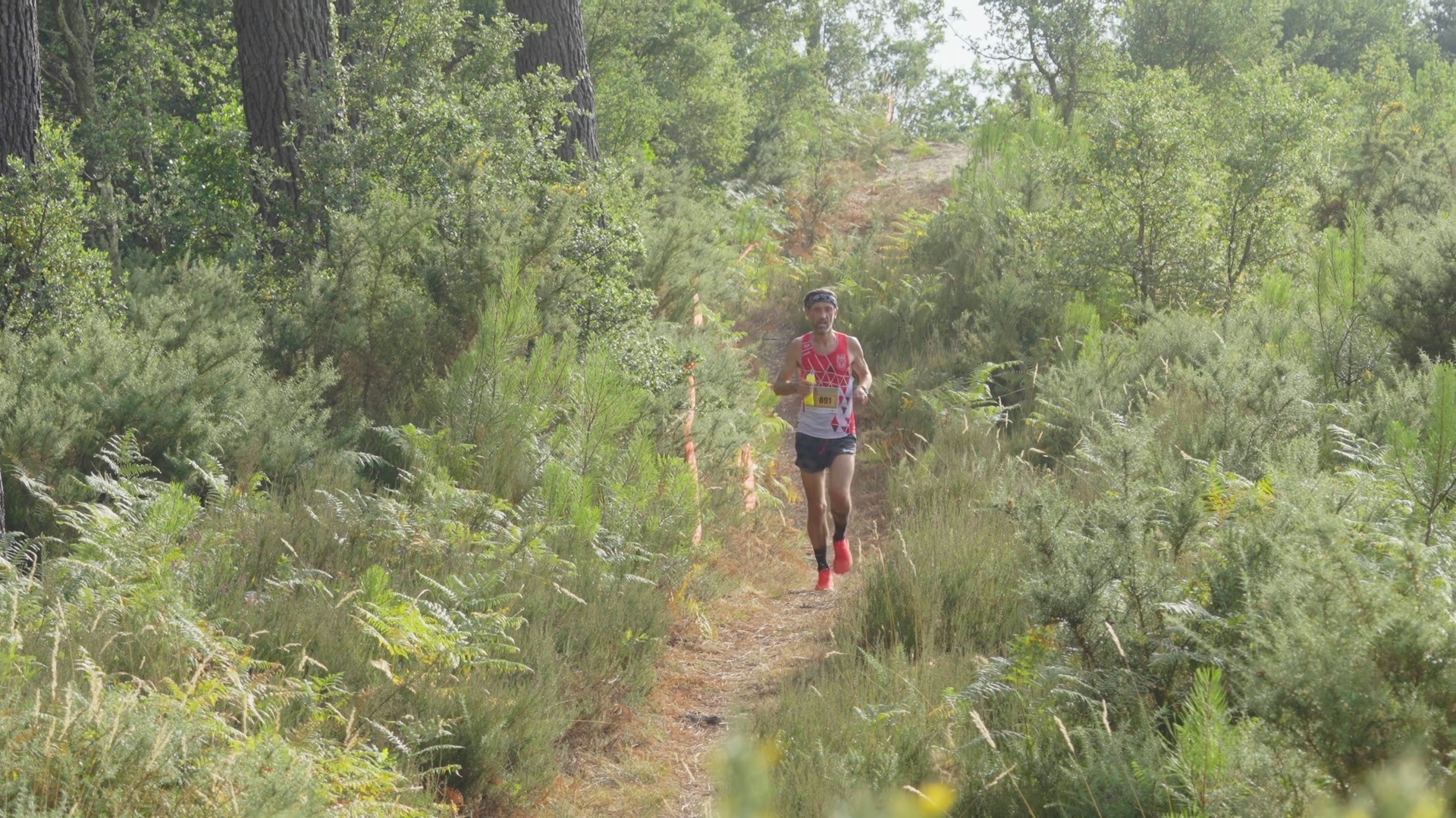 Coureur en maillot rouge et blanc en descente dans les fougères